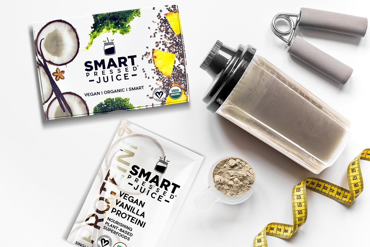 top view of a smart pressed vegan vanilla proteini, a cup of powdered proteini, a tape measure, a plastic container containing proteini and a hand grip on top of a white table.