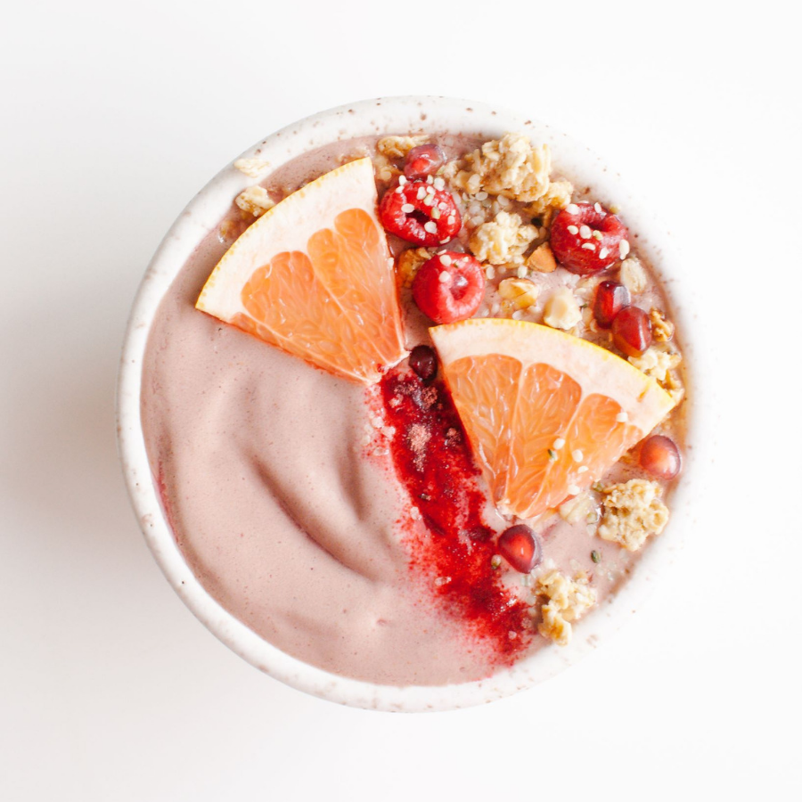 top view shot of a bowl of frozen Revive Beet+Root smoothie topped with 2 slices of orange and sprinkled with raspberries and nuts.