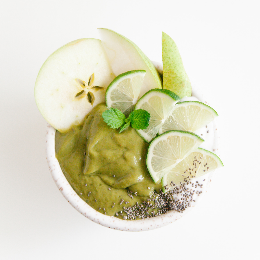 top view of matcha greens smoothie Bowl topped with slices of lemon, three slices of pear with chia and mint in the middle