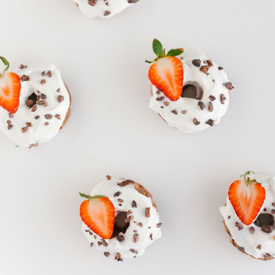 4 donuts with white coating sprinkled with chocolate crumbs and a slice of strawberry on a white surface.