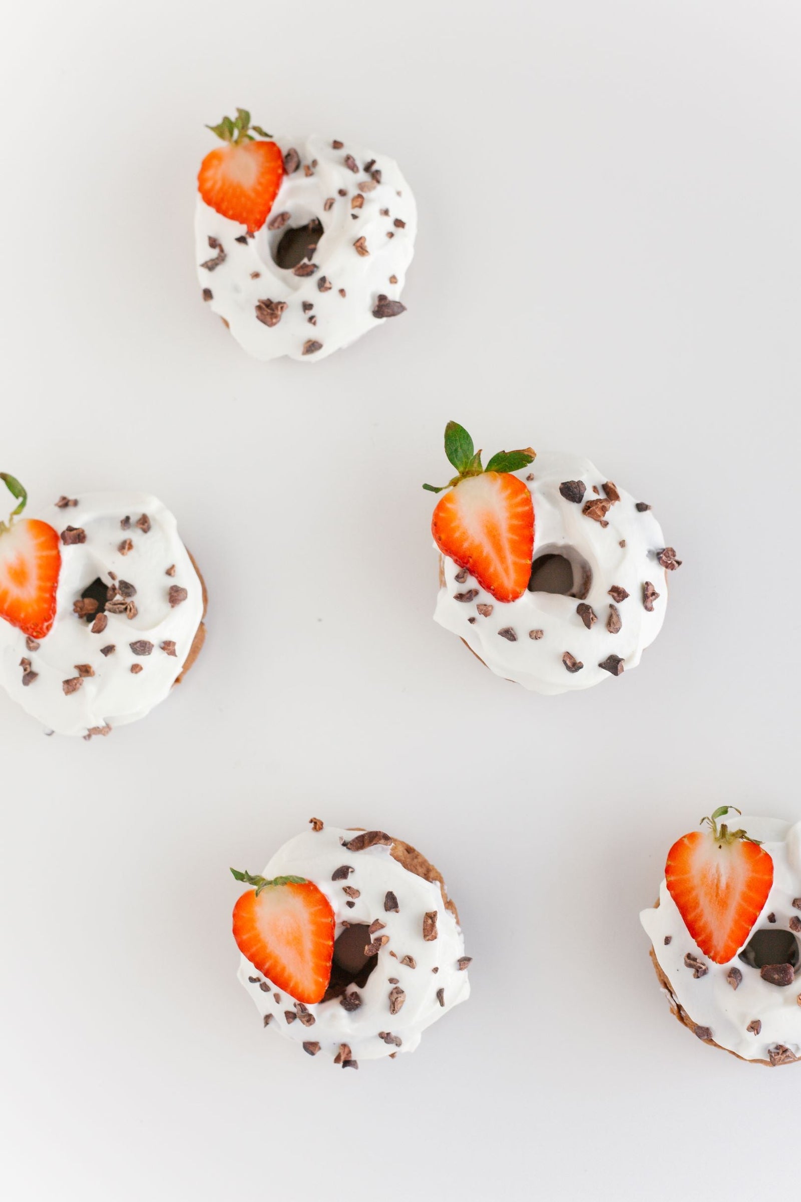 top view of a glasses of proteini topped with whip cream and a slice of strawberries and choco bits on top of a white table