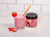 a glass of strawberry beets smoothie garnish with strawberry with a brown paper straw and smart beetroot labeled jar on the side and slices of strawberry on top of a white table