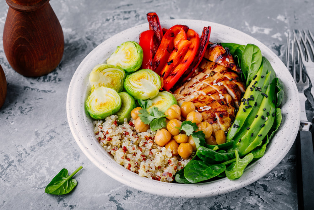 top view of a ceramic bowl with Hardy Bowl of Goodness with a leaf of arugula and two forks on the side with two wooden condiments container on top of a marble table