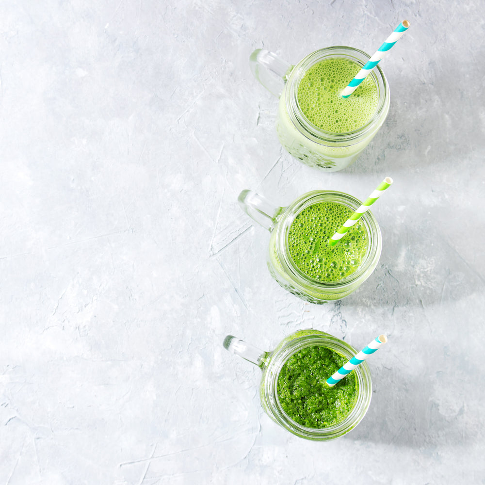 top view of three glasses of mixed banana, avocado, and mango smoothie with two blue and green patterned paper straw on top of a table