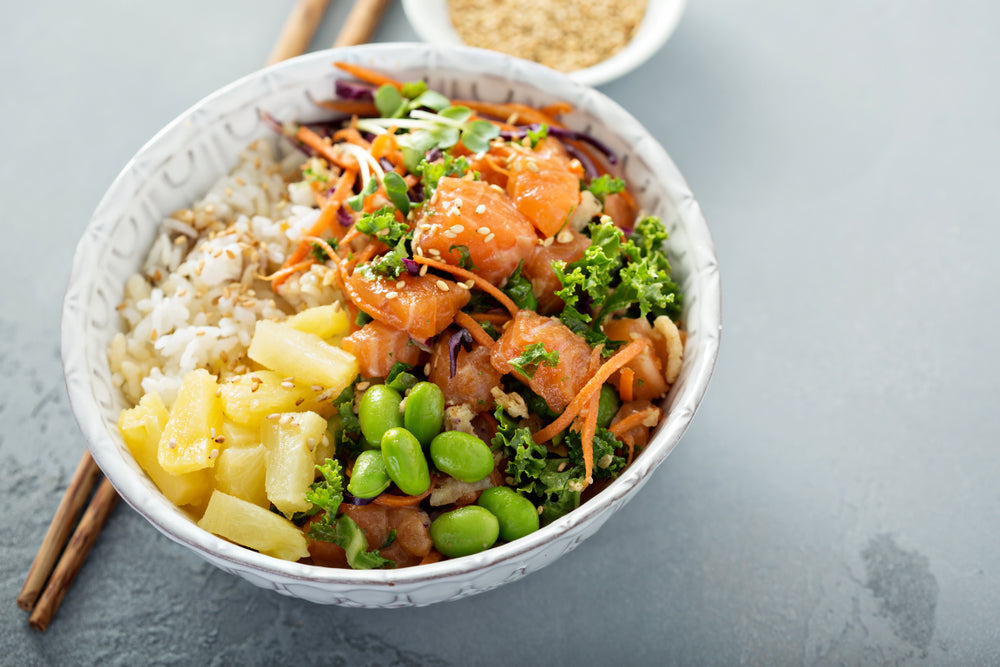 top view of a ceramic bowl with pineapple-ginger rice bowl with chopsticks on the side a small bowl of sesame seeds on top of a blue-painted table