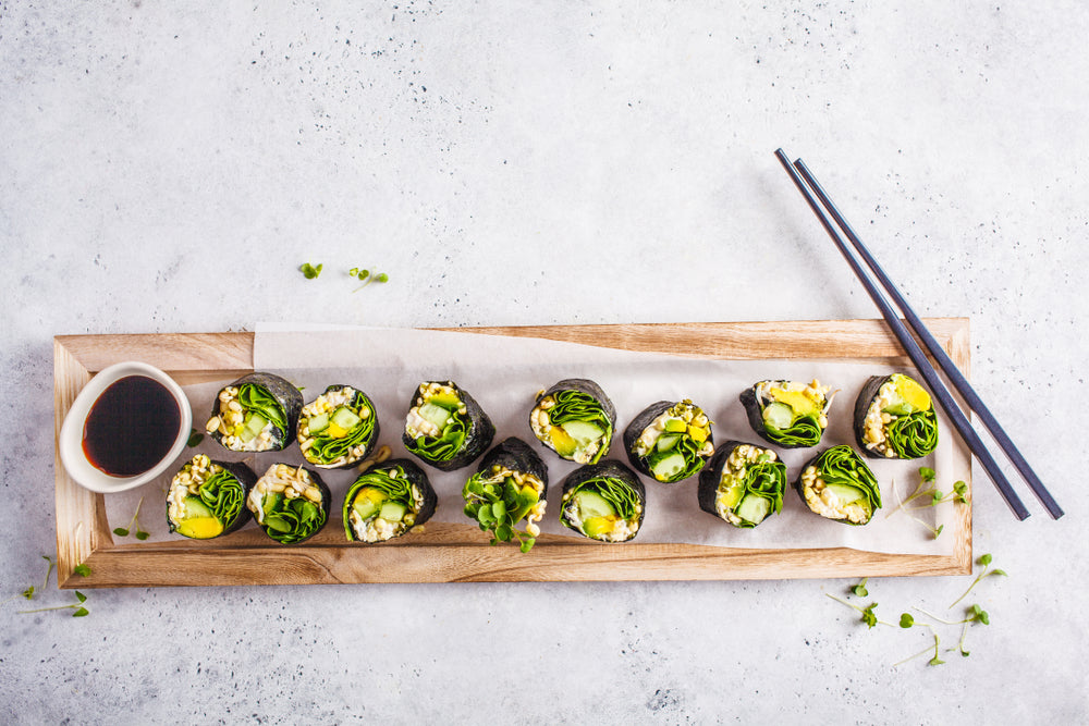 top view of rice-free sushi with sauce and chopsticks on the side with parchment paper at the bottom on top of a wooden plank on top of a white table