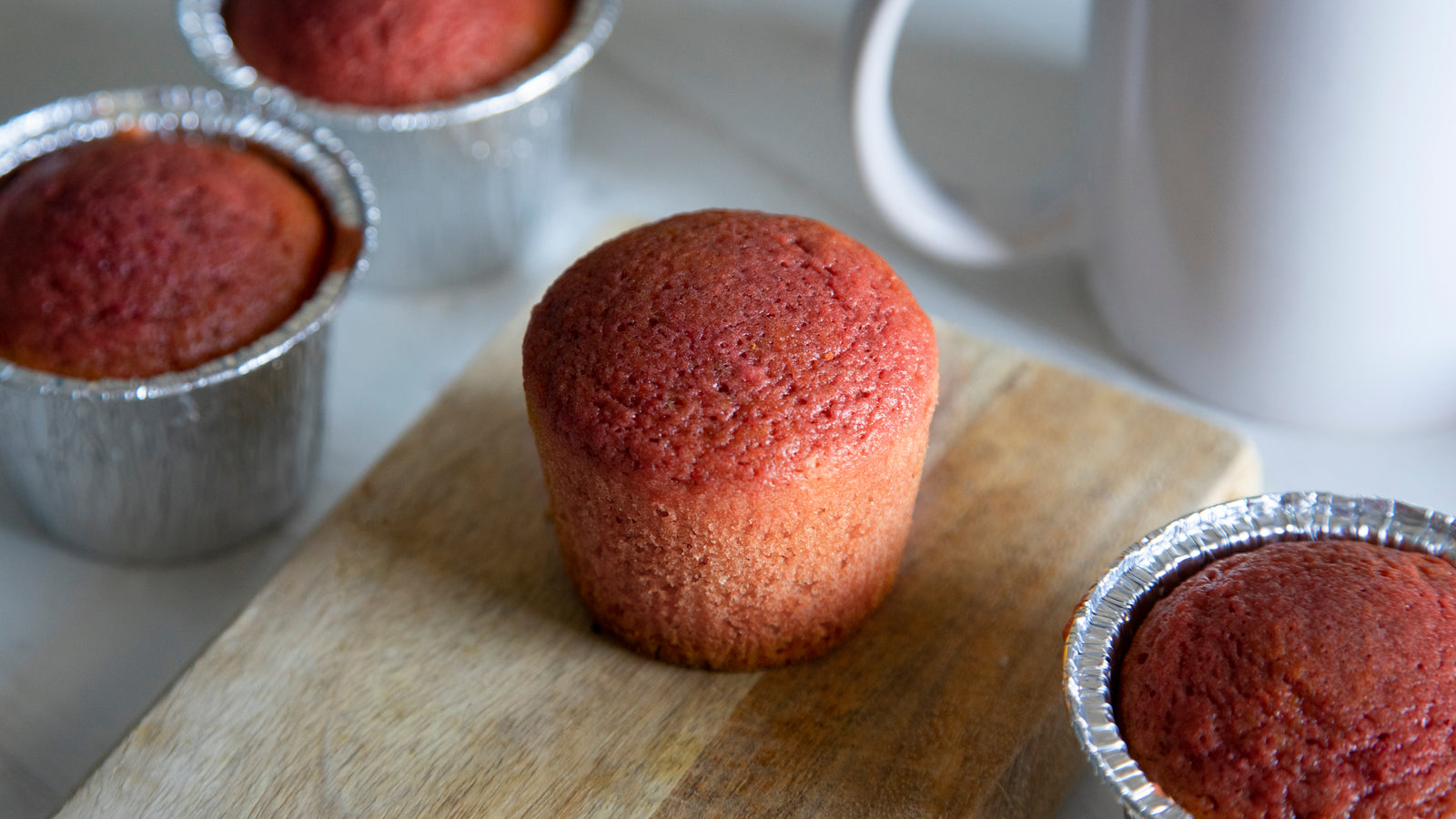 four pieces of red velvet beet cupcakes, one was placed on a wooden chopping board with no aluminum molder and a white coffee cup