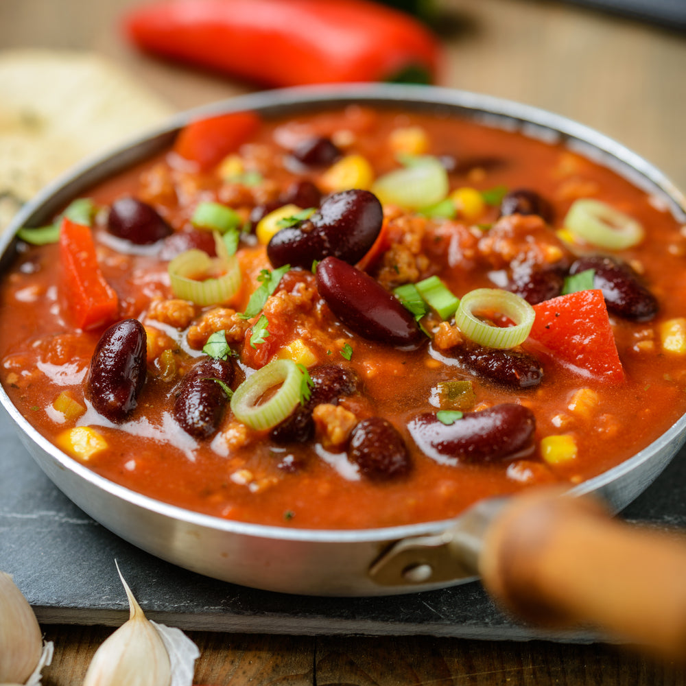 a skillet full of savory mushroom soup with red beans, corns kernels, garnished with chopped leeks