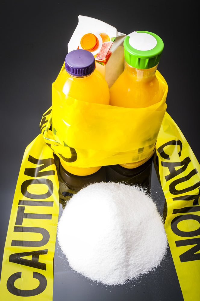 two bottles and a tetra pack of orange juice tied together by a yellow caution printed sash and a lump of sugar in front on top of a black table