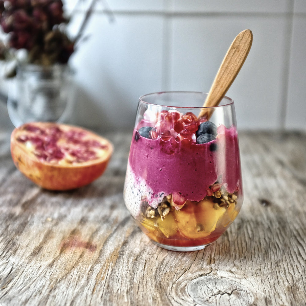 A glass of Blueberry Pomegranate Acai Smoothie with a wooden spoon, next to a pomegranate