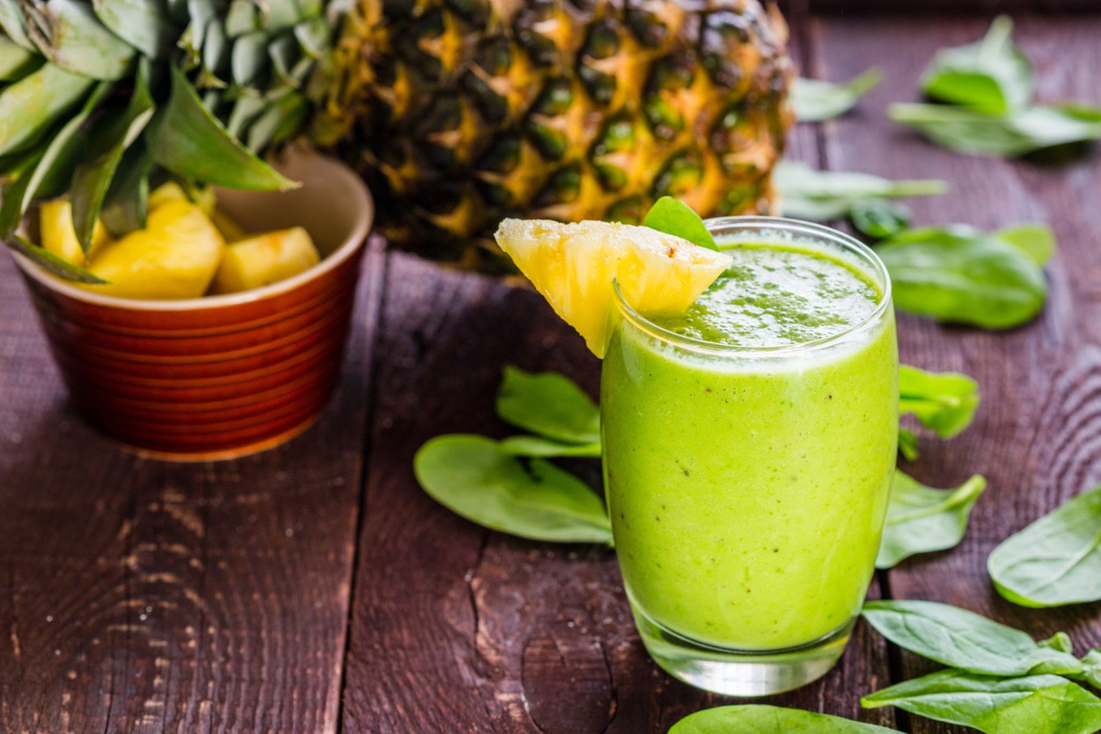 image of pineapple, pineapples in red cup, and a glass of a green smoothie with a pineapple wedge