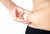 Image of a woman's hand pinching her belly fat, set against a white background.
