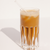 a glass of Iced Protein Coffee with transparent straw reflecting its shadow on a white background