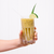 a close-up hand holding a glass of Pineapple Chia Fresca garnished with a sliced lime and pandan leaf with transparent straw.
