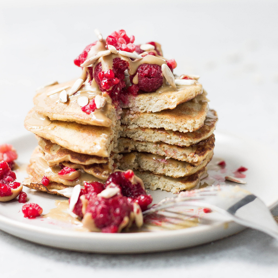 pancakes on a white plate topped with pomegranate and nuts.