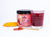 a jar of Revive Beet+Roots beside a glass of Revive Beet+Roots juice, on the surface is a spoon with pink powder and a slice of turmeric, Set against a white background. 