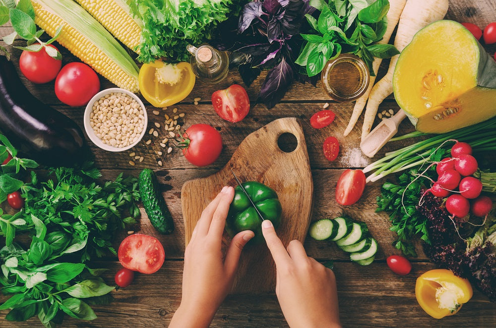 Image of hands cutting a green bell pepper on a cutting board surrounded by fresh vegetables and whole grains.