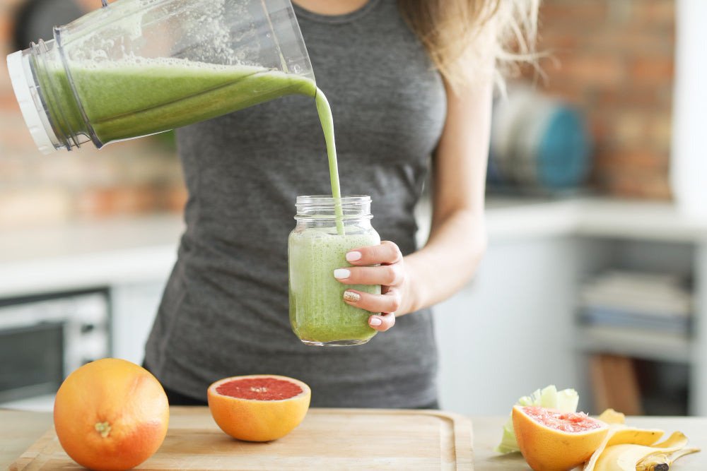 Woman holding a blender with green smoothie putting some in a glass jar