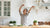 Image of a happy woman  in her kitchen, waving her hands in the air.