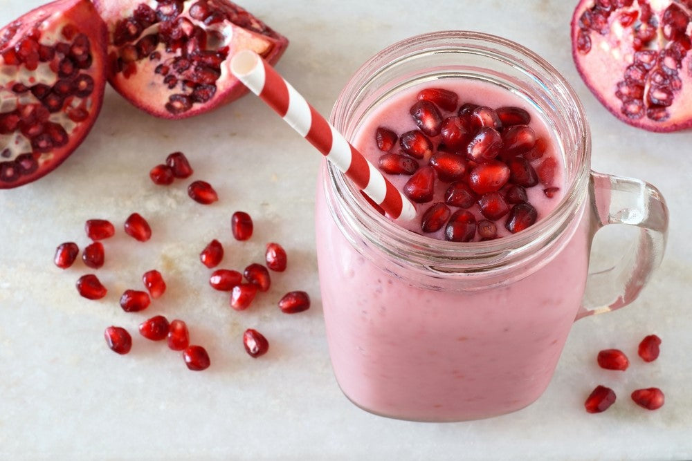 Royal Pomegranate Sorbet Smoothie in a jar with straw with pomegranate seeds scattered under it