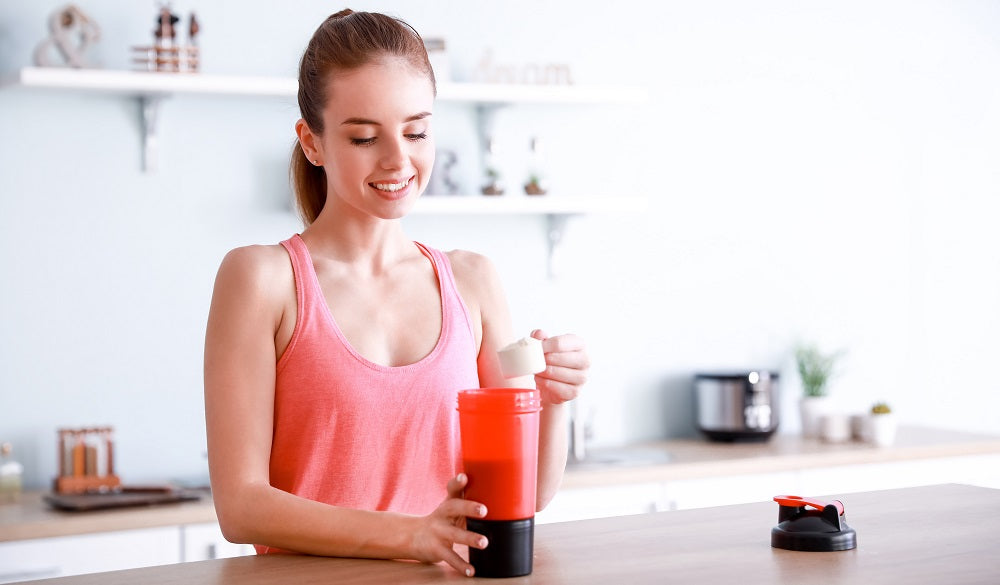 Image of a happy woman on her kitchen top, making a smoothie in her tumbler.
