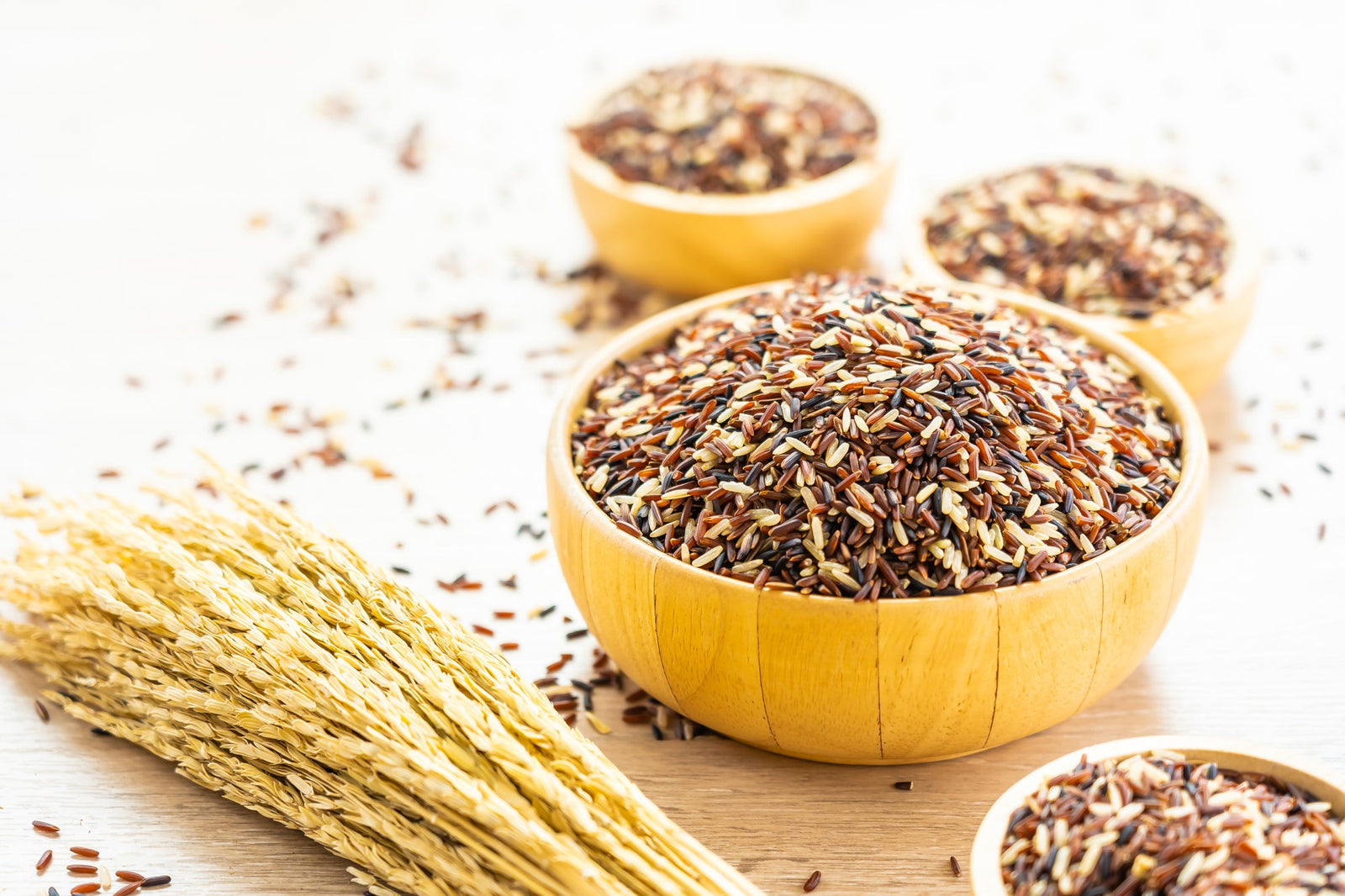 Image of 1 big and 3 smaller yellow bowls full of brown grains, On the surface is some rice stalk and scattered rice.