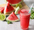 a glass of watermelon chia refresher garnished with a slice of watermelon and a blue patterned paper straw with slices of watermelon on top of a wooden chopping board with a slice of lime and mint leaves on the side