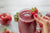 a hand holding a glass of strawberry apple smoothie garnished with strawberry and apple, grapes and strawberries side by side