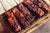 top view of a griller with five BBQ tempeh with sweet potatoes on sticks on top of a wooden table