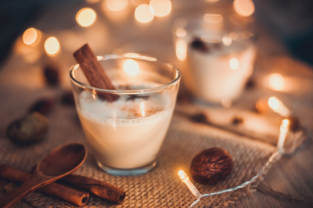 a glass half-filled with vanilla bourbon pineapple chia smoothie with a vanilla stick and two vanilla sticks on the side with a wooden spoon on top of it surrounded by Christmas lights