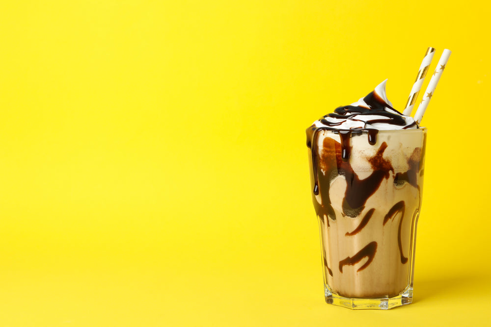 Chocolate milkshake with chocolate syrup and whipped cream and two straws in a tall glass on a yellow background