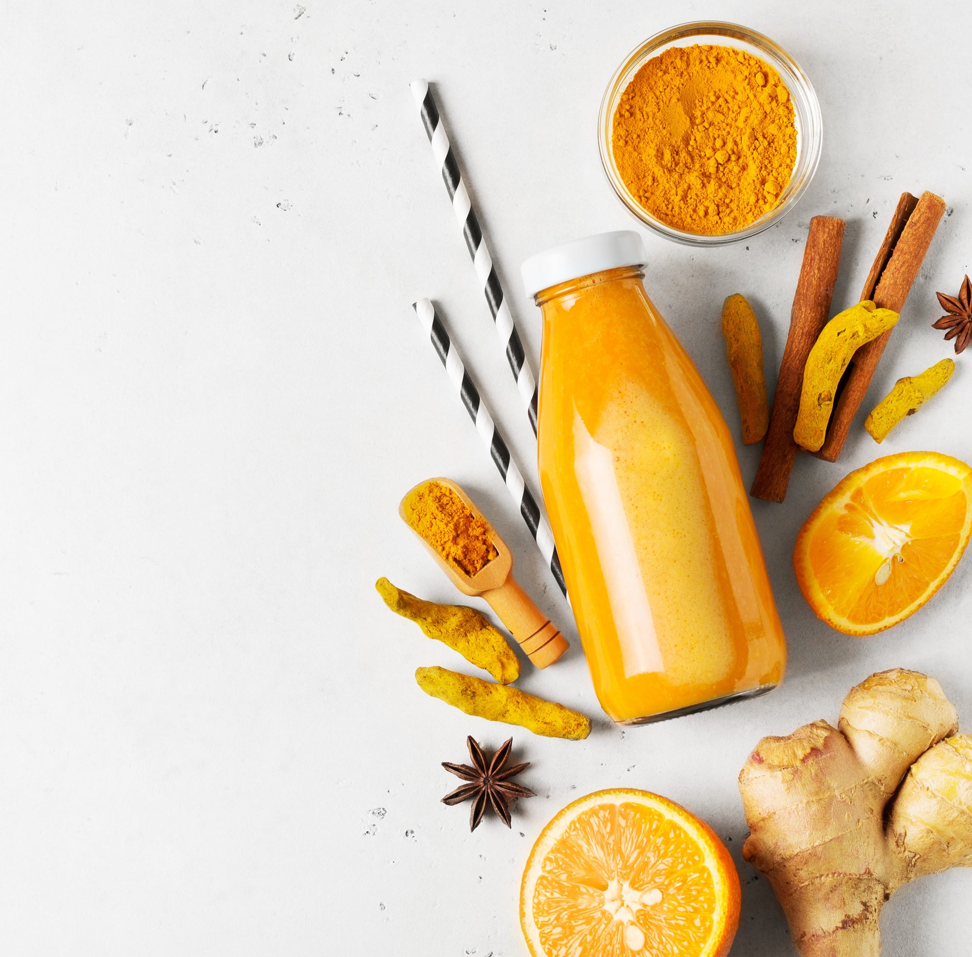 1 jar of Tami's Anti-Inflammatory Smoothie beside 2 straws, 1 small bowl of turmeric powder, cinnamon sticks, turmeric, 2 slices of oranges, ginger, and star anis on a white background.