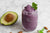 Avocado next to glass of purple berry smoothie with a mint leaf
