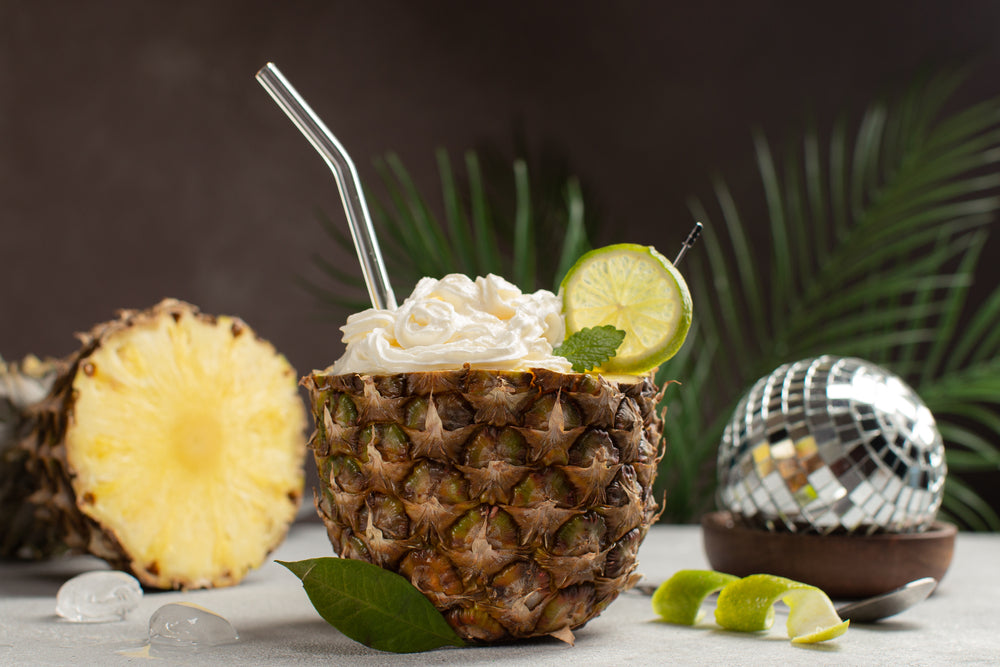 A serve of Pineapple Whip Debloating Smoothie inside a pineapple, next to a disco ball and pineapple