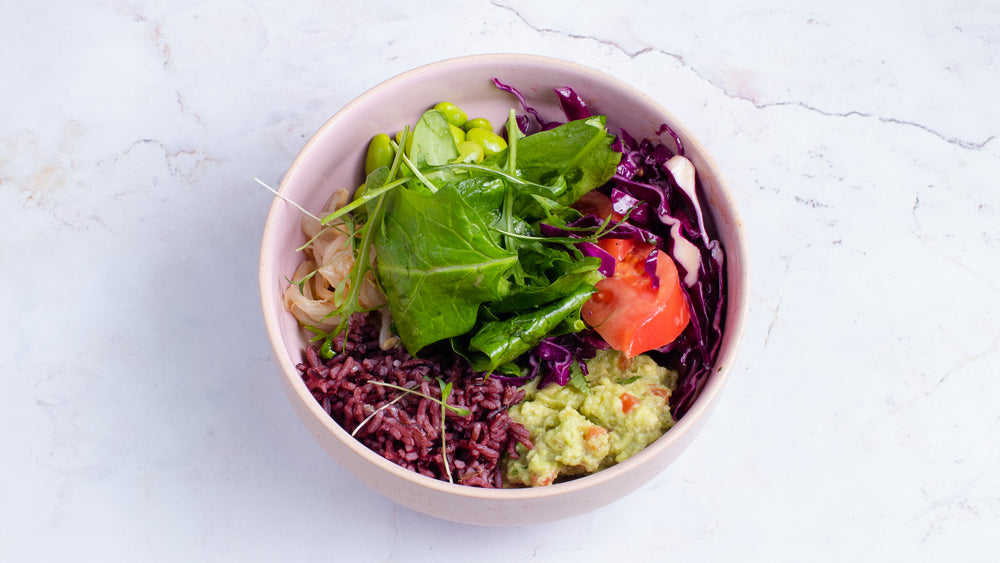Purple rice, avocado, assorted vegetables prepared in a pink bowl over a marble background