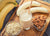 top view shot of a glass of Vegan Vanilla Proteini smoothie with a straw beside 2 peeled bananas, a bowl of almond nuts, a bowl of oats on a wooden cutting boards and beside 3 bananas. 