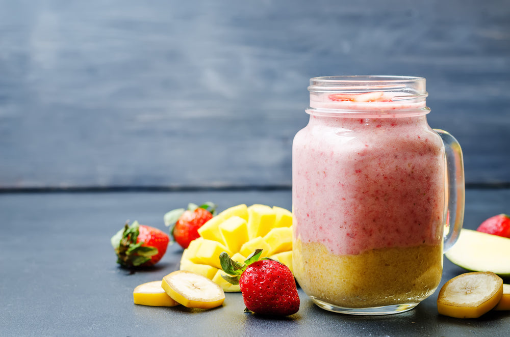 a jar of strawberry mango Smoothie surrounded by sliced mango, slices of banana, and strawberries 