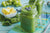 side view of two mason jars filled with pressed greens blueberry lemon smoothie topped with berries on top of a stripe folded table cloth surrounded by a bunch of spinach, a small bowl of slices of pineapple, and grapes on top of a table 