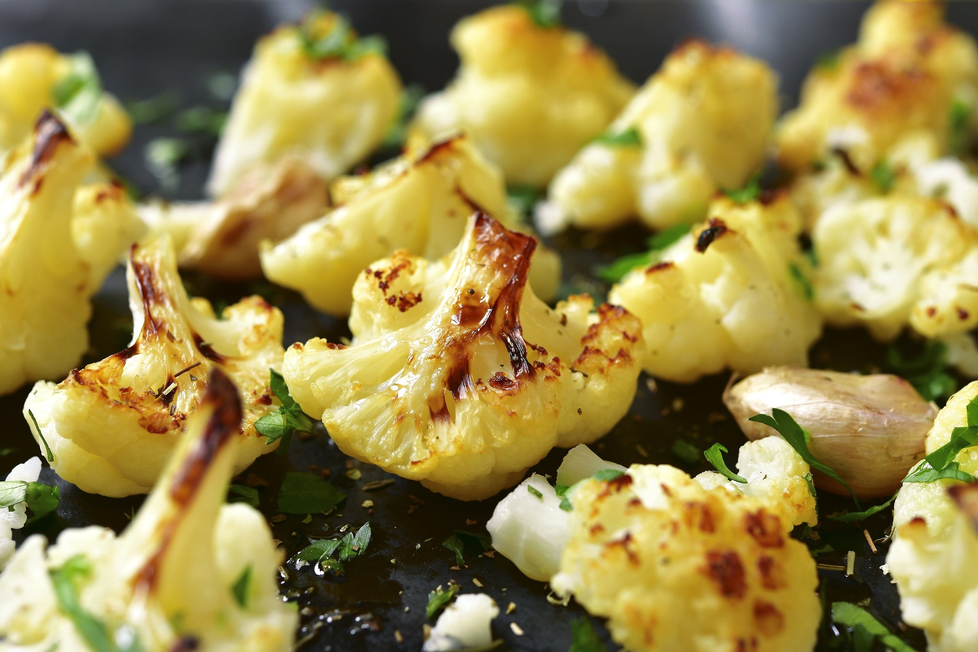 close-up shot of roasted cauliflowers sprinkled with chopped green herbs in a pan.