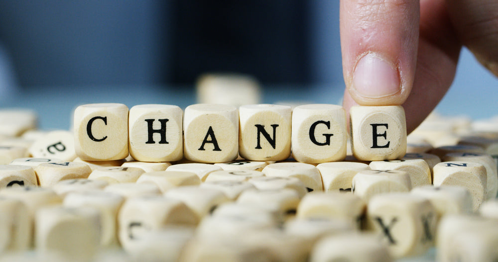 Collection of small dice with the word CHANGE on it and a finger pinning a dice with a letter E surrounded by different letters of dices.