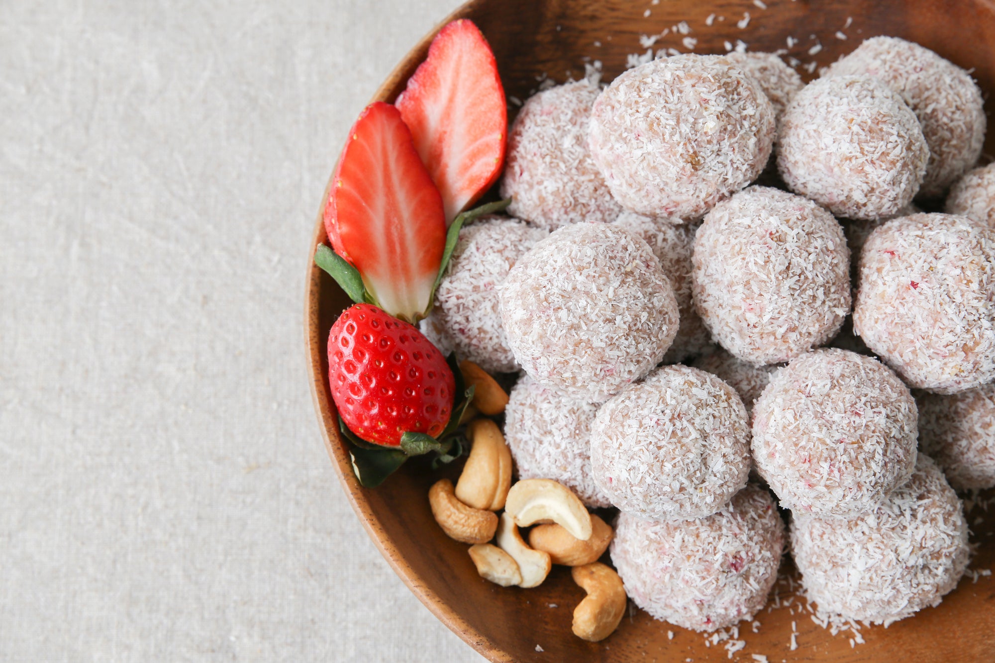 top view of strawberry chia balls with cashew nuts and slices of strawberries on the side inside of a wooden bowl