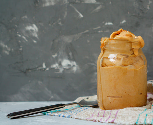a jar of chocolate peanut butter smoothie on top of a table cloth with a spoon on the side