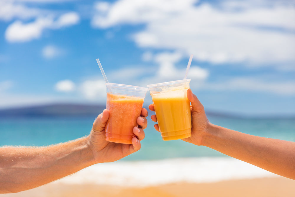two hands holding a glass of tropical coconut smoothie with plastic transparent straw at the seashore