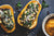 top view of two pieces of half sliced roasted kabocha with cranberry kale stuffing and a bowl of mashed kabocha on top of a blue-painted wooden table
