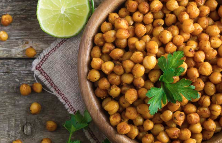 top view image of a bowl of chickpeas garnished with parsley. On the surface is a slice of lemon, some chickpeas, and parsley. 