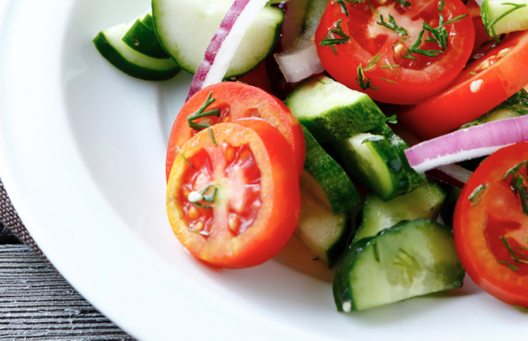 a plate of tomato and cucumber salad garnished with green herbs and sliced red onion.