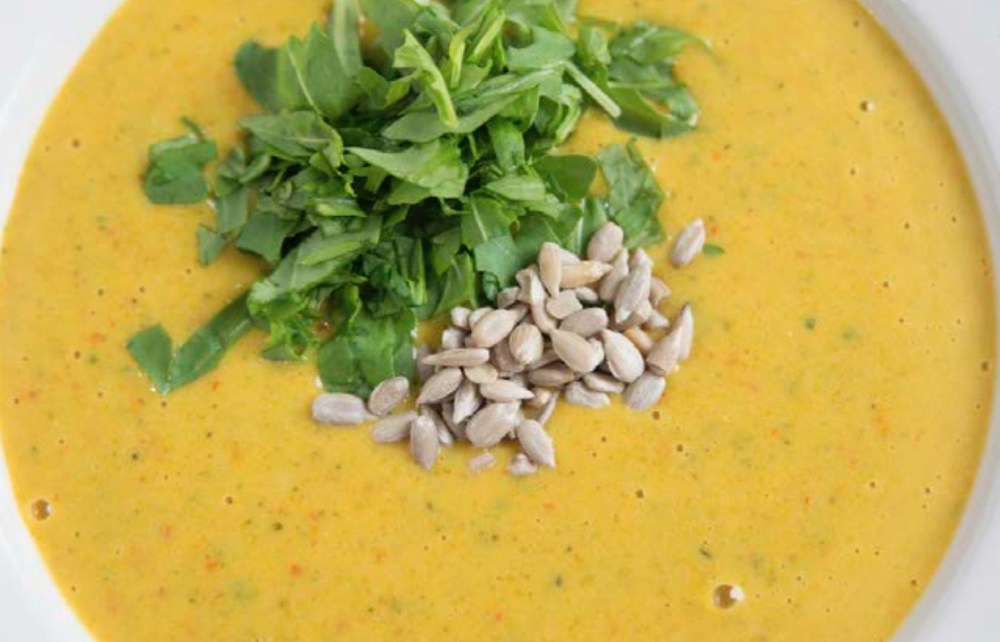 top view shot of a bowl of yellow coconut curry soup topped with sunflower seed and chopped cilantro.