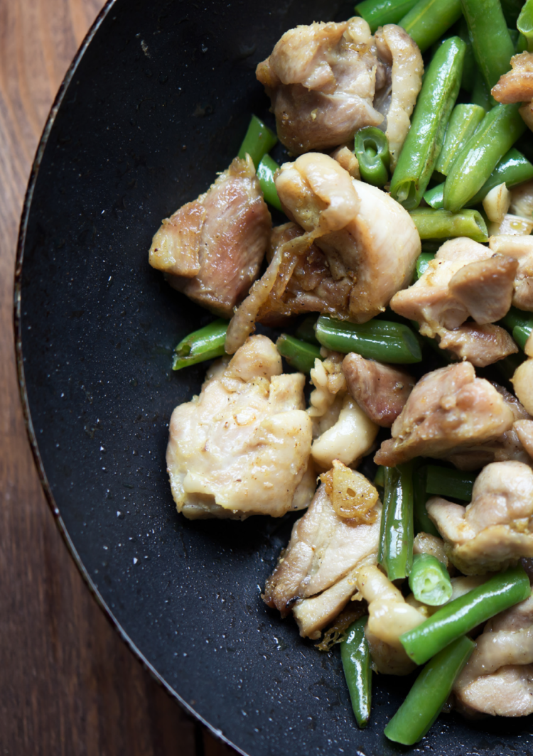 top view shot of a wok with sliced green beans and chopped chicken breast. 