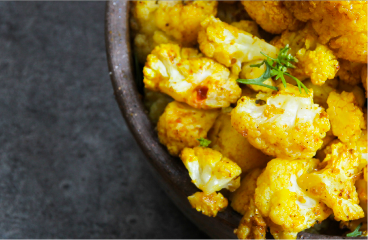 a bowl of cooked cauliflower garnished with green herb
