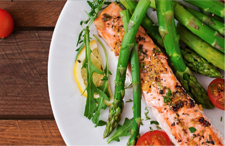 top view shot of a plate of seared salmon with asparagus, a slice of lemon, and sliced cherry tomatoes on a wooden surface